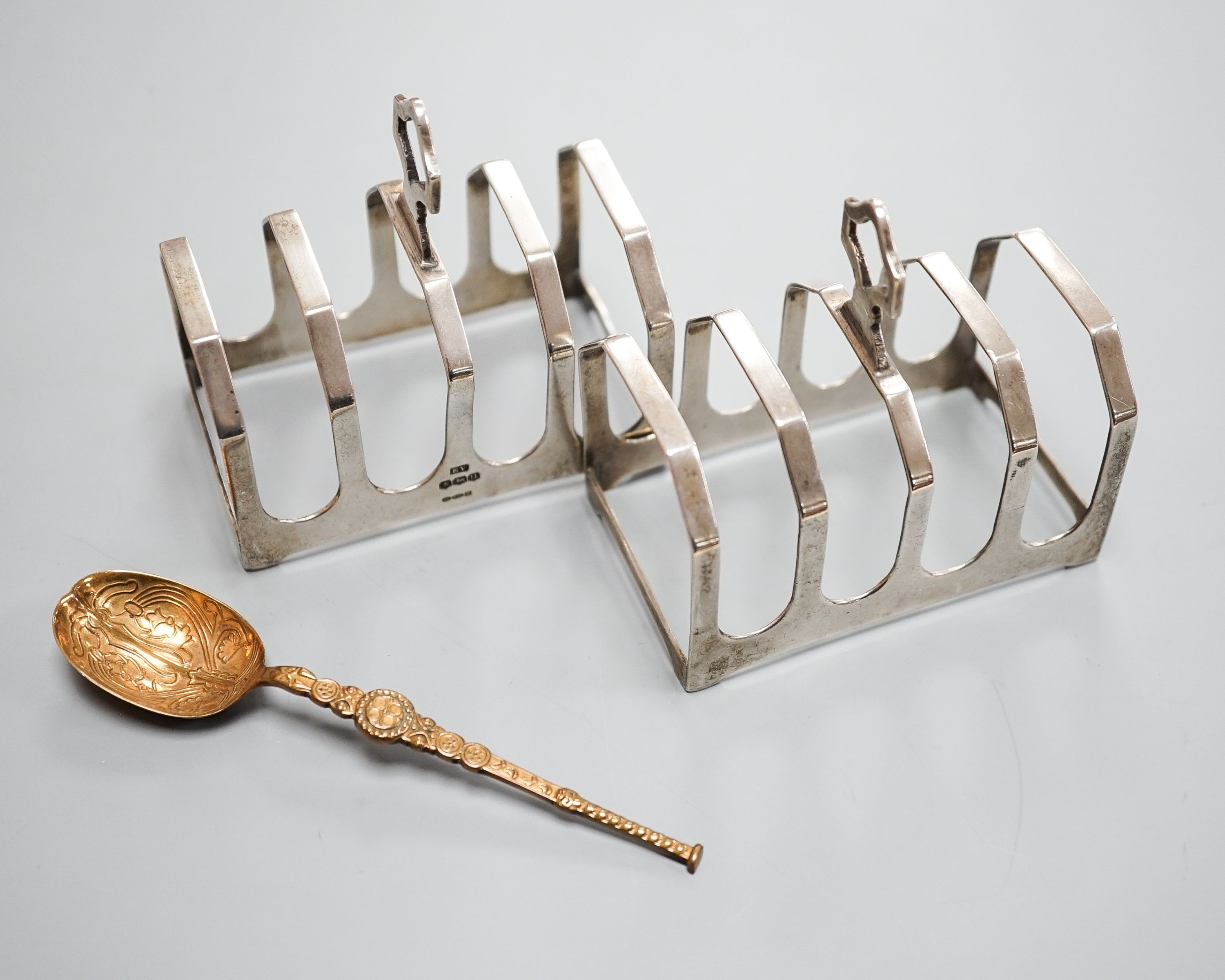 A pair of George VI silver five bar toastracks, Viner's Ltd, Sheffield, 1937, length 76mm and metal replica of a 12th century Coronation spoon.